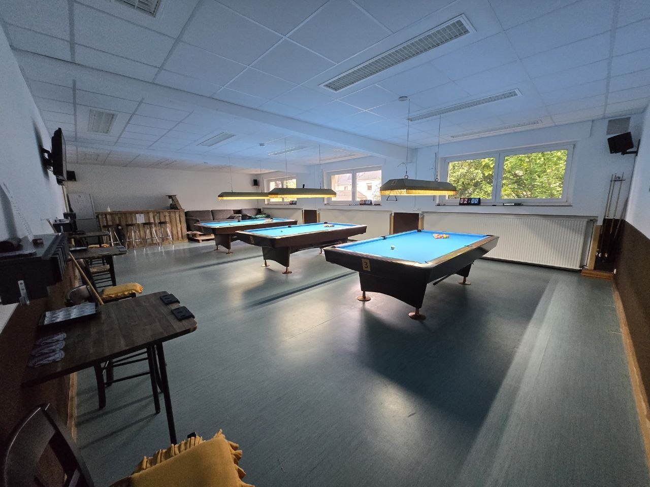 Vereinssaal mit drei blauen Pooltischen, Stühlen und Fernseher an der Wand